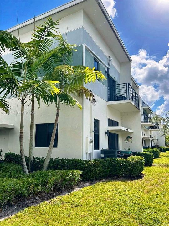 Contemporary multi-level exterior featuring smooth stucco siding, private balconies with metal railings, and integrated landscape hedging