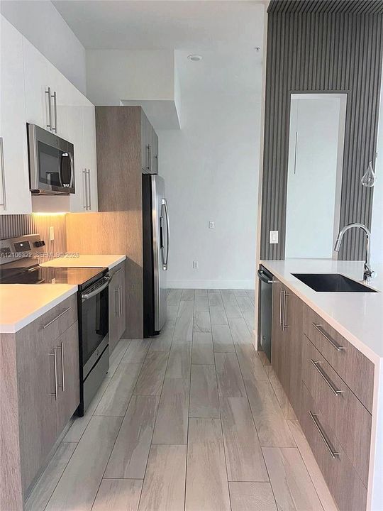 Kitchen featuring flat-panel cabinetry with wood-finish and high-gloss white upper doors, stone-finish countertops, stainless steel appliances, and vertical slat wall detailing