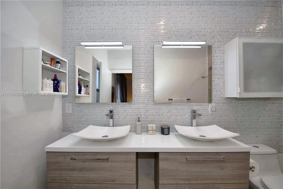 Double vanity with wood-finish cabinetry, white countertop, dual vessel sinks, chrome faucets, and tiled wall backsplash