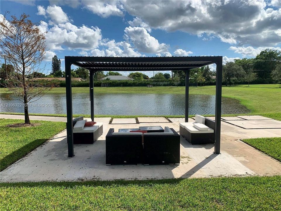 Outdoor living area featuring a black metal pergola, concrete paver patio, and natural waterfront setting