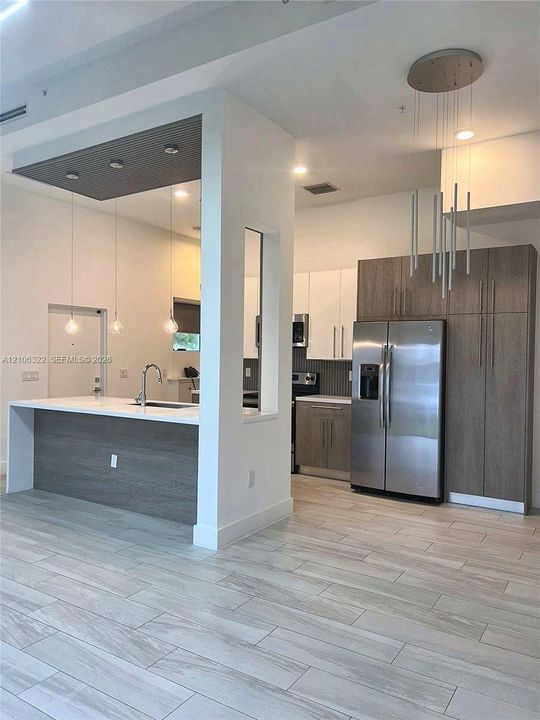 Kitchen featuring dual-toned flat-panel cabinetry, a waterfall-edge island with integrated sink, wood-finish flooring, and multi-pendant lighting fixtures