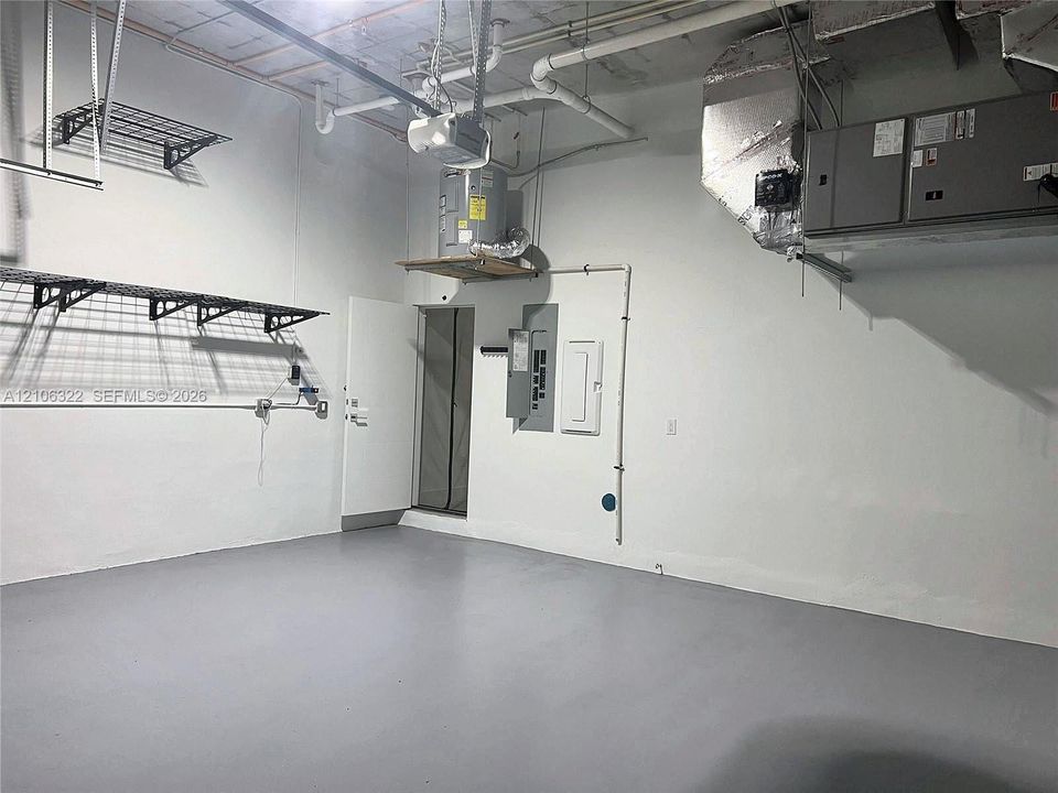 Finished garage space with epoxy-coated flooring, white interior walls, mounted wire shelving, ceiling-mounted HVAC unit, and an elevated water heater