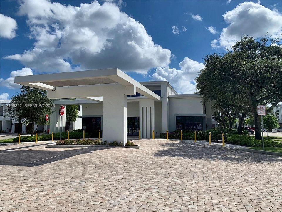 Modern architectural facade with a prominent cantilevered porte-cochère, paver driveway, vertical accent detailing, and perimeter bollard lighting