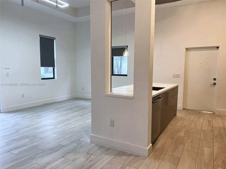 Kitchen featuring wood-finish cabinetry, quartz countertops, stainless steel dishwasher, wood-finish flooring, and a cut-out partition