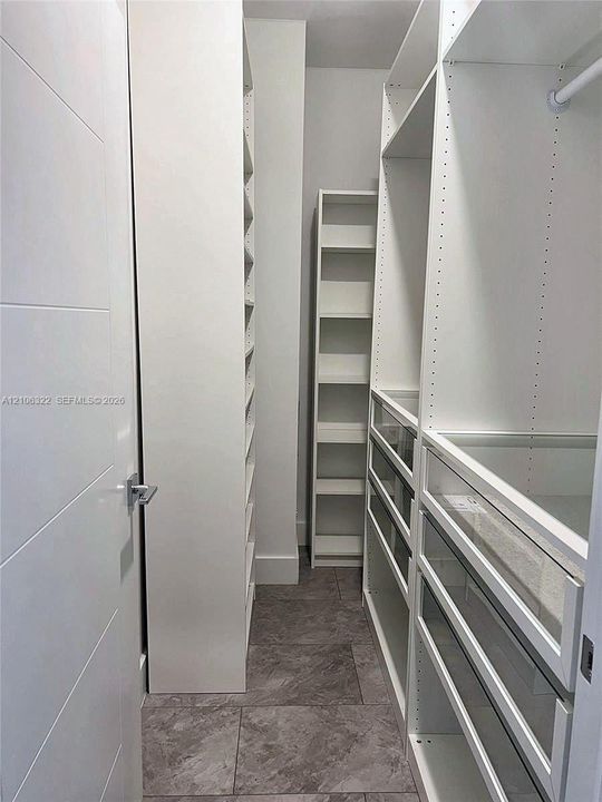 Custom walk-in closet featuring white built-in shelving, glass-front drawers, hanging rods, and stone-finish tile flooring