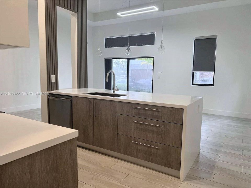 Kitchen island featuring a white surface, flat-panel wood-finish cabinetry, a stainless steel undermount sink with a gooseneck faucet, and integrated lighting