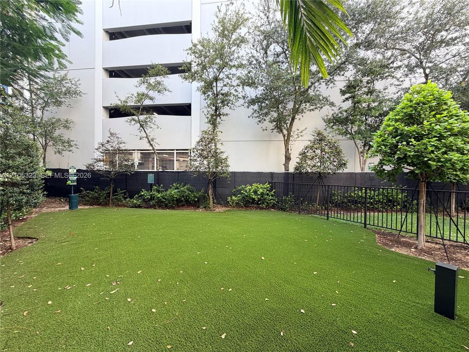 Ground-level outdoor space featuring synthetic turf, mature perimeter trees, and black metal perimeter fencing
