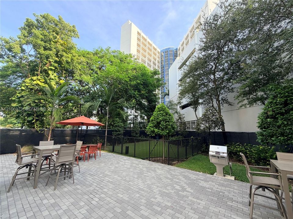 Paver patio featuring a built-in outdoor grill and a fenced grassy area with mature trees