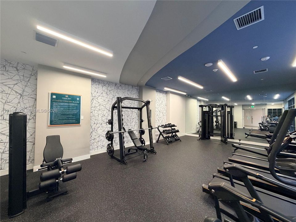 Fitness center featuring black rubberized flooring, floor-to-ceiling mirror walls, recessed ceiling lighting, and patterned accent wall covering