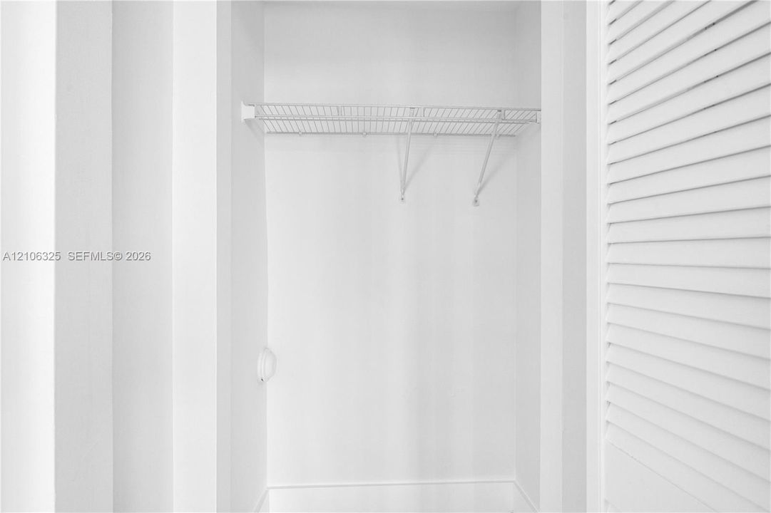 Storage closet featuring white louvered doors and white wire shelving