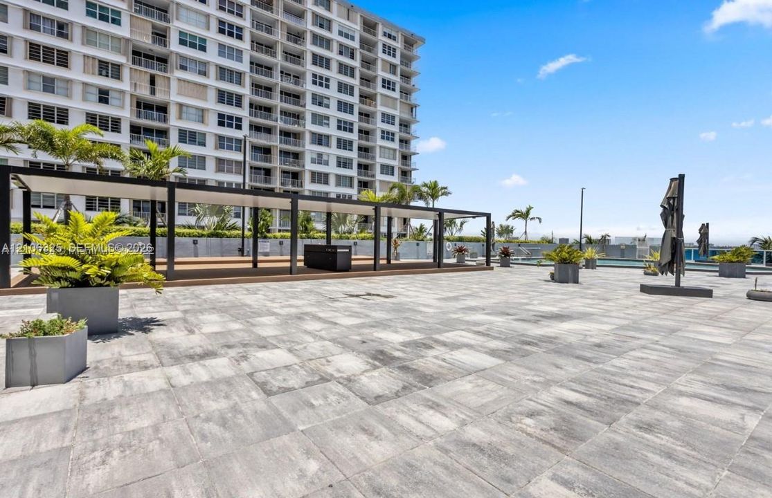 Expansive outdoor terrace featuring stone-tiled flooring, a large structural metal pergola, and perimeter landscaping