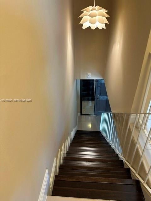 Staircase featuring wood-finish treads, white metal railing, and a tiered petal-style pendant light fixture