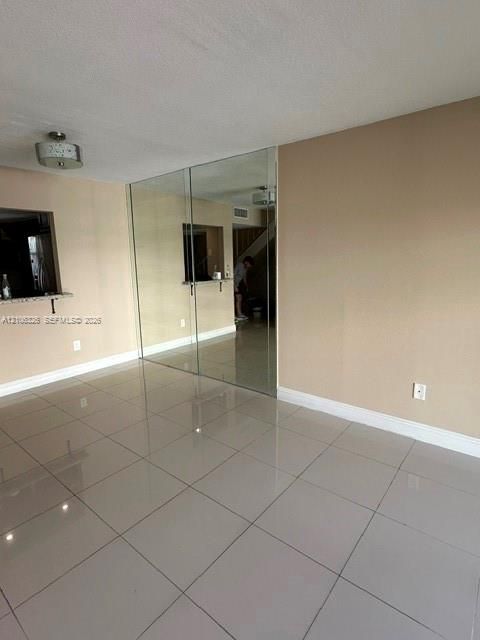 Neutral tile flooring, large floor-to-ceiling mirror panel, pass-through opening with stone-finish ledge, and contemporary drum-style ceiling lighting