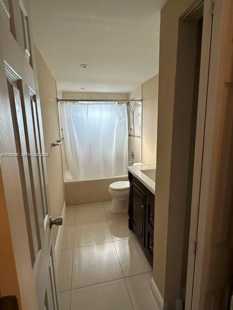 Bathroom featuring large-format tile flooring, a dark wood-finish vanity with a white countertop, and a shower-tub combination with light-toned wall tile
