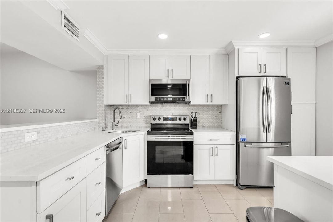 Kitchen featuring white shaker-style cabinetry, stainless steel appliances, quartz countertops, mosaic tile backsplash, and ceramic tile flooring