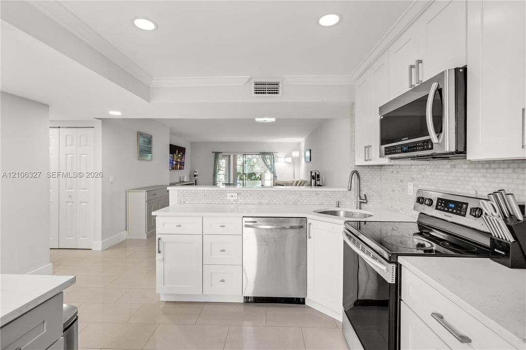 Kitchen featuring white shaker-style cabinetry, stainless steel appliances, neutral stone-finish countertops, mosaic tile backsplash, and recessed lighting