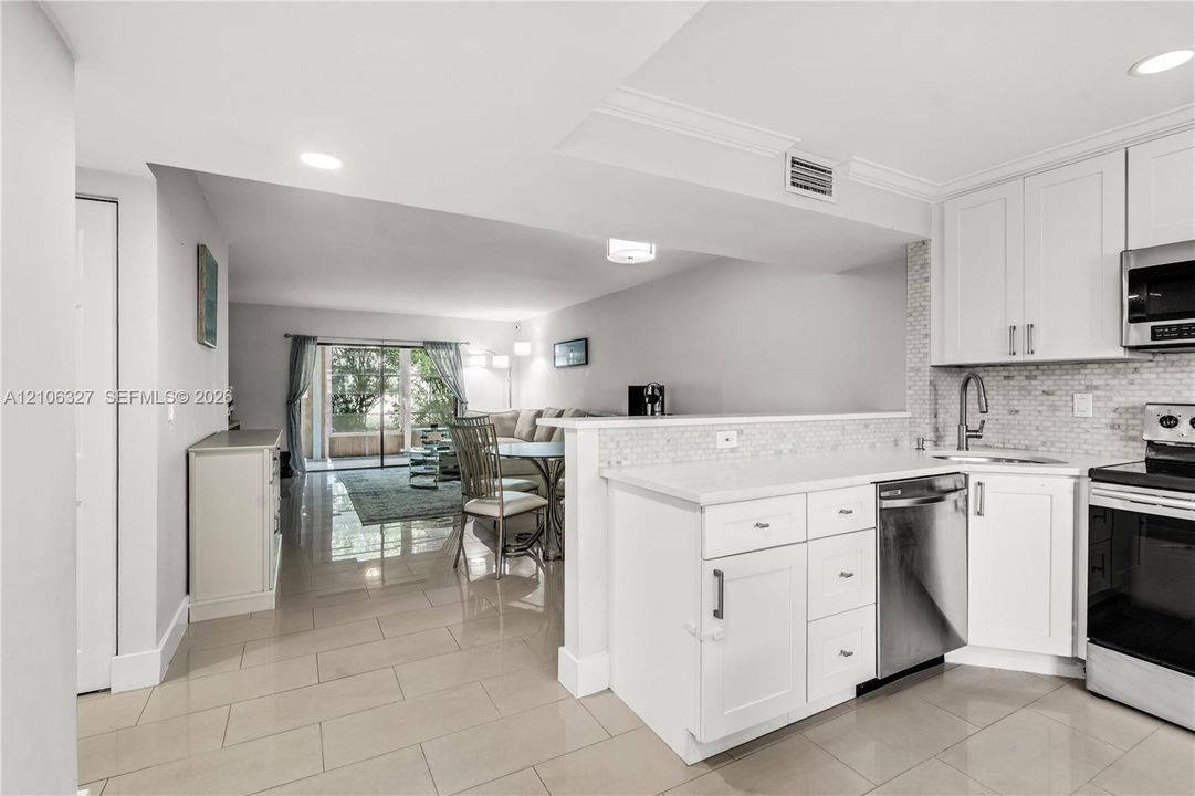 Kitchen featuring white shaker-style cabinetry, a mosaic tile backsplash, stainless steel appliances, and large-format tile flooring