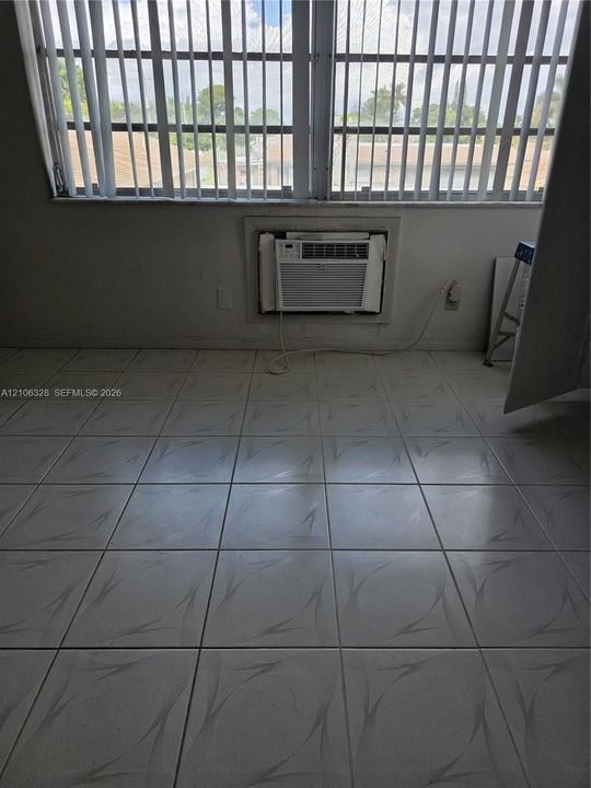 Large-format tile flooring, oversized horizontal window with vertical blinds, and wall-mounted air conditioning unit
