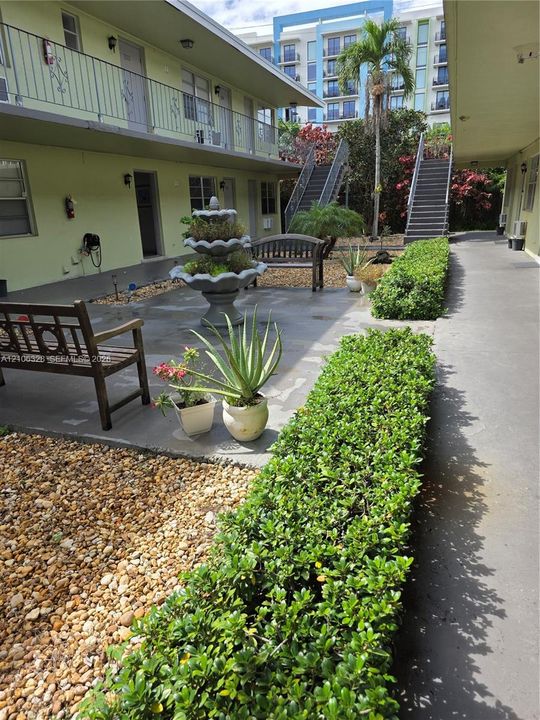 Courtyard area featuring a tiered stone fountain, concrete patio, gravel landscaping, and maintained shrubbery