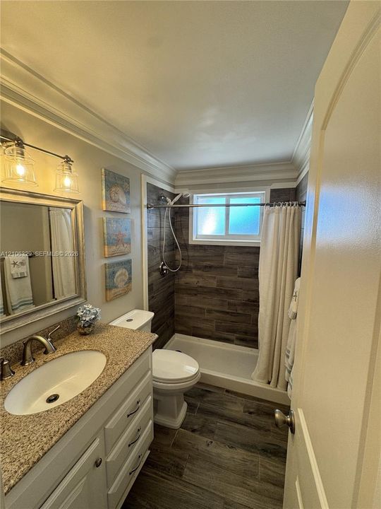 Bathroom featuring a stone-composite countertop, white vanity cabinetry, wood-finish flooring, and wood-finish tile shower surround