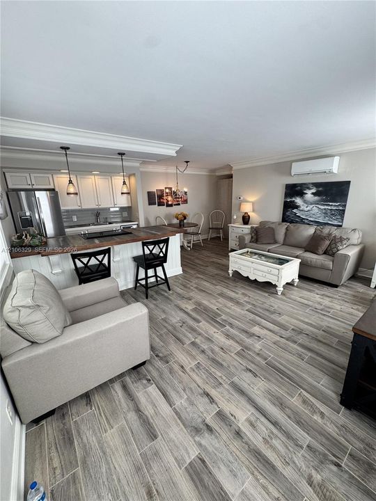 Open-concept area featuring wood-finish tile flooring, white cabinetry with crown molding, a breakfast bar with a wood countertop, and dual pendant lighting