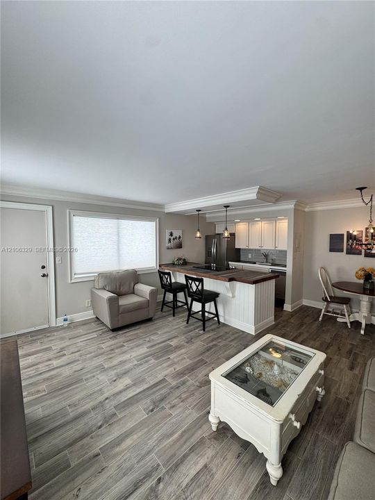 Wood-finish flooring, kitchen island with wood-tone countertop, white shaker-style cabinetry, crown molding, and pendant lighting