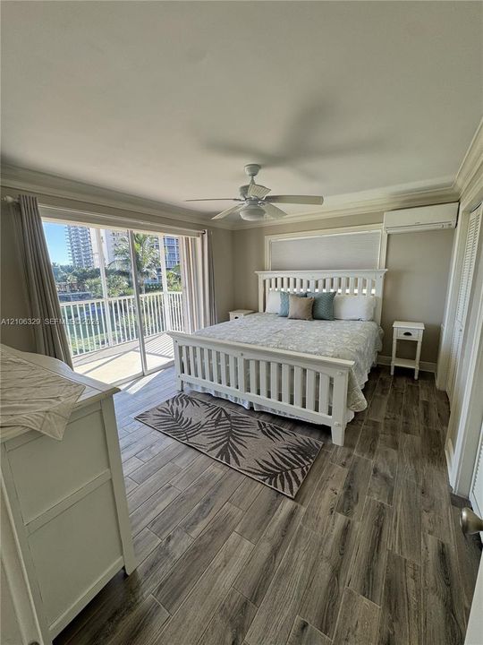 Wood-finish tile flooring, ceiling fan, crown molding, wall-mounted air conditioning unit, and sliding glass doors with balcony access