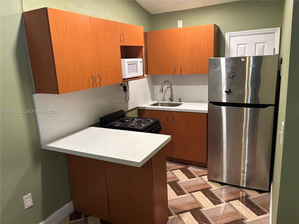 Kitchen featuring wood-finish cabinetry, solid surface countertops, stainless steel refrigerator, and geometric-patterned flooring