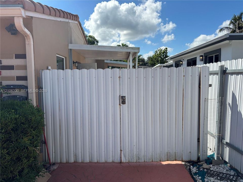 Exterior white corrugated metal privacy gate with a locking handle, attached to a white vinyl perimeter fence
