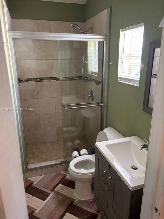 Walk-in shower featuring glass sliding doors and tile surround, single-sink vanity with cabinet storage, and patterned tile flooring