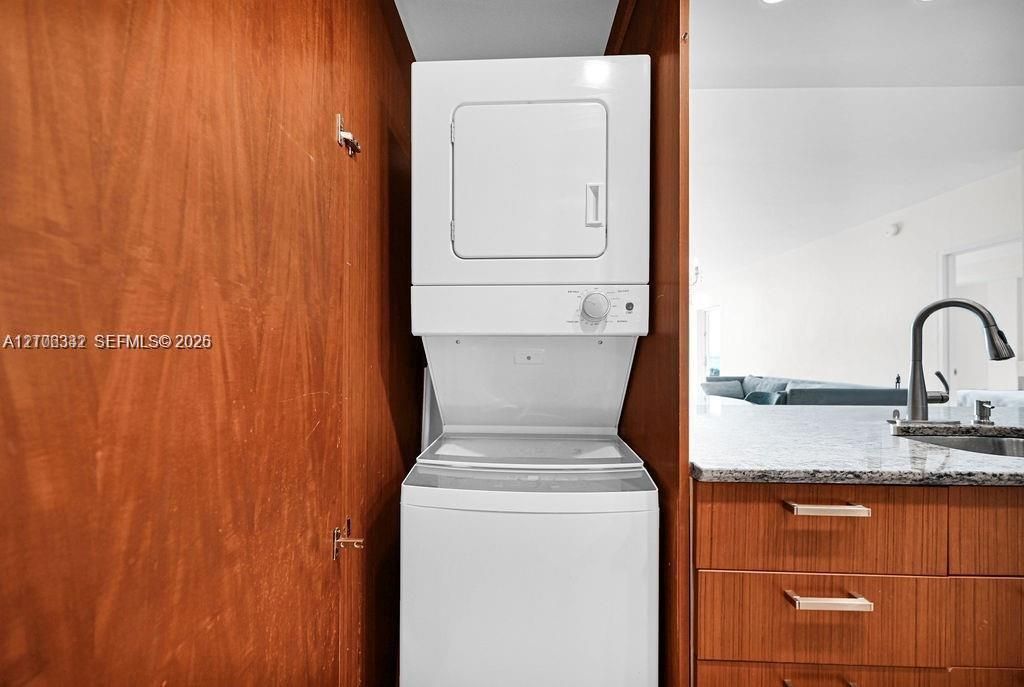 Stacked laundry unit housed within wood-finish cabinetry, featuring stone-surface countertop, flat-panel drawers with horizontal hardware, and a high-arc pull-down faucet