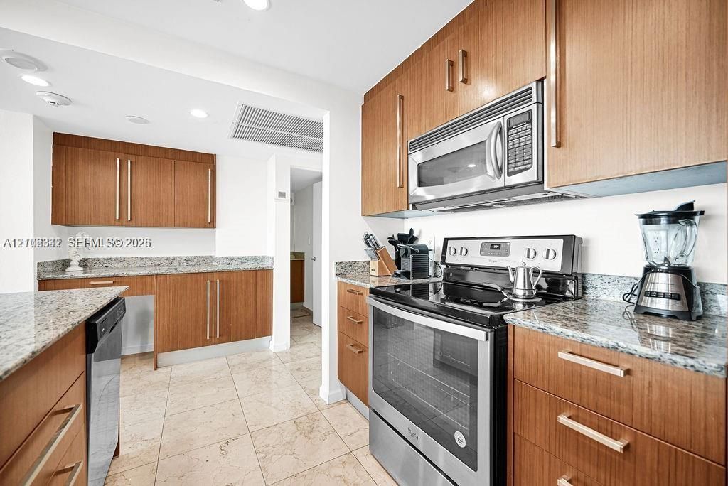 Kitchen featuring wood cabinetry, stone countertops, stainless steel appliances, and tile flooring