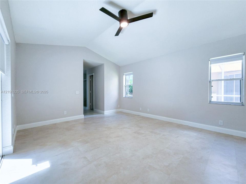 Vaulted ceiling, matte black three-blade ceiling fan with integrated lighting, neutral large-format tile flooring, and multiple dual-pane windows