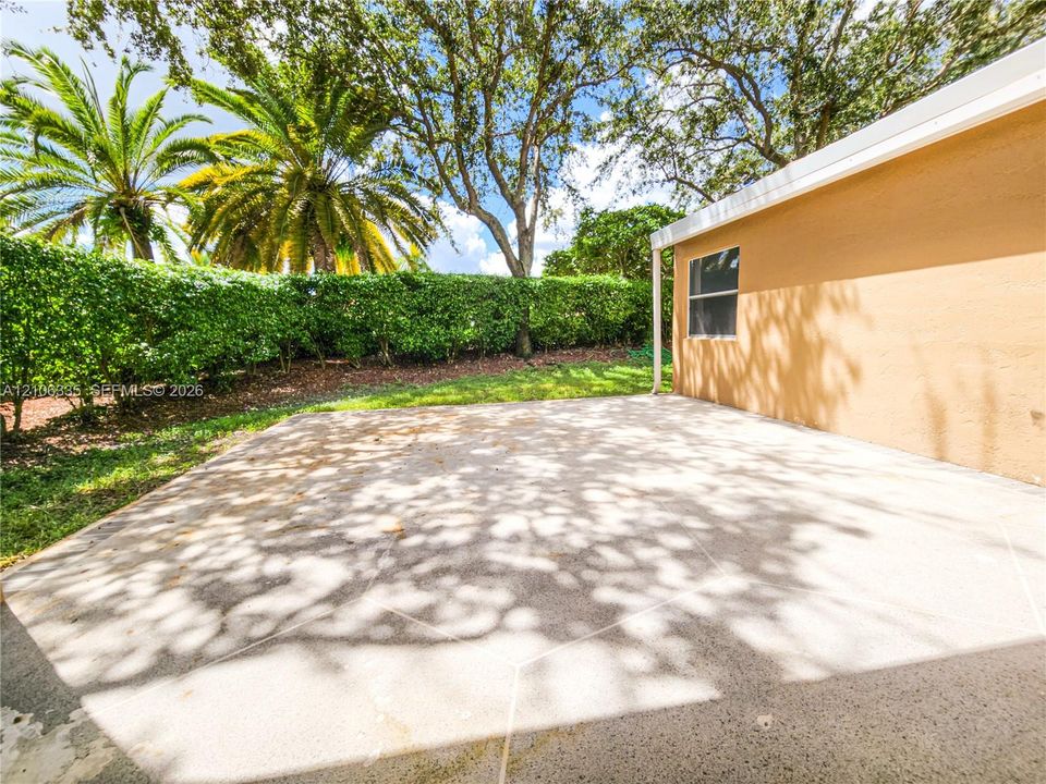 Concrete patio with stucco exterior wall, perimeter privacy hedge, and mature trees
