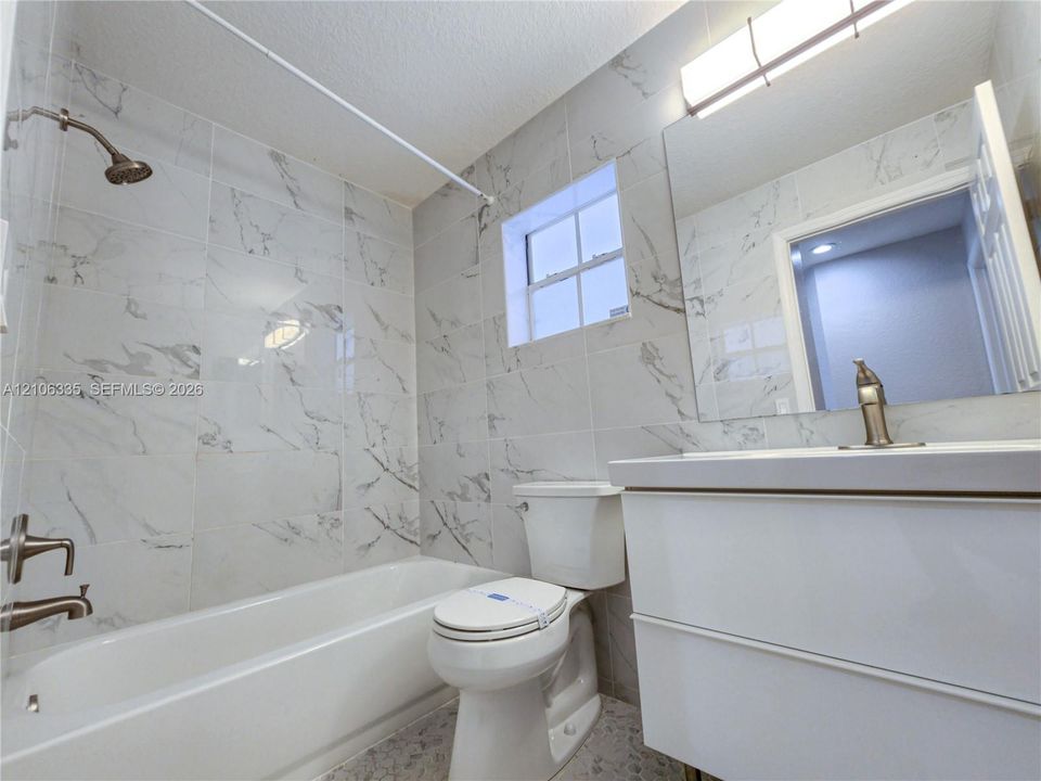 Bathroom featuring floor-to-ceiling veined tile, white vanity with integrated basin, polished metal hardware, and full-width vanity mirror with integrated lighting