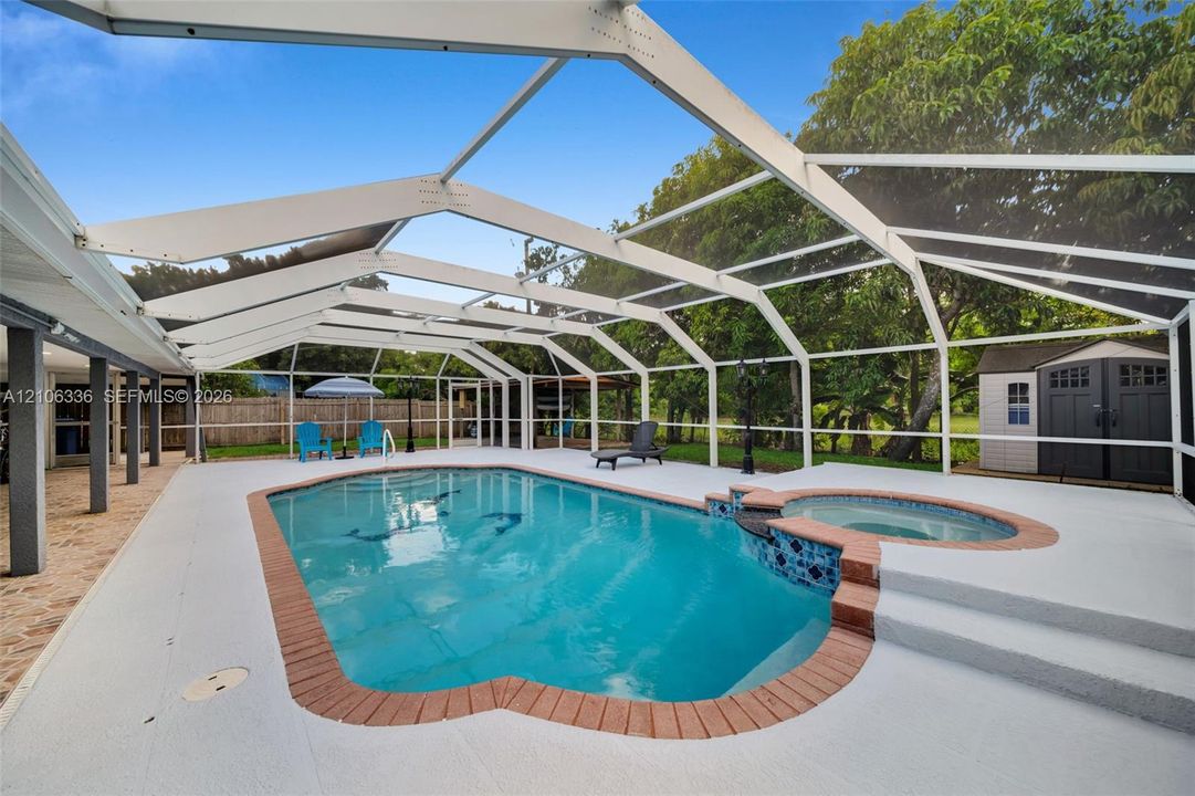 Screened-in pool area featuring an attached elevated spa, brick paver coping, and expansive concrete decking