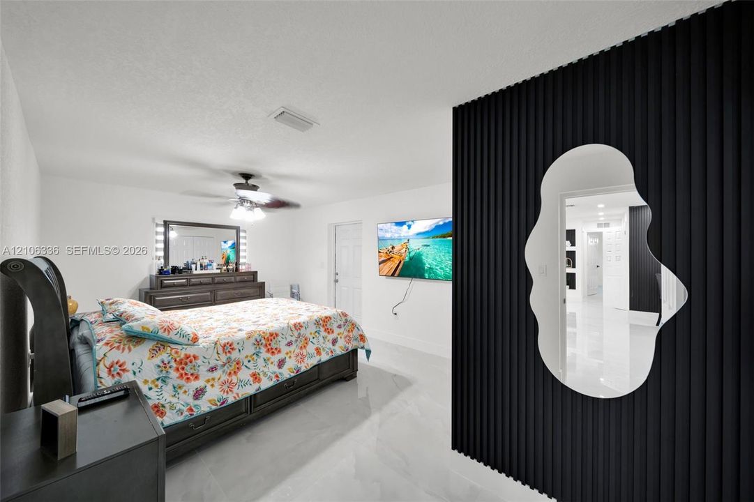 Black vertical slat accent wall with a custom-shaped wall mirror, high-gloss tile flooring, and a ceiling-mounted fan with integrated lighting