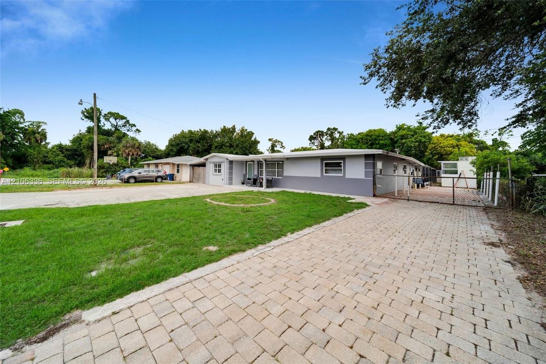Single-story residence featuring a two-tone exterior, extensive paver driveway, gated side access, and a manicured lawn