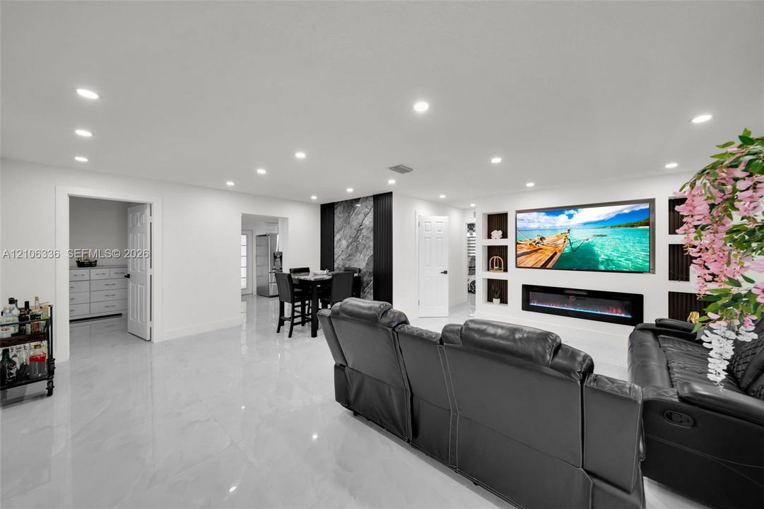 Open-concept living space featuring high-gloss tile flooring, recessed lighting, a built-in electric fireplace, recessed wall shelving, and an accent wall with stone-finish cladding