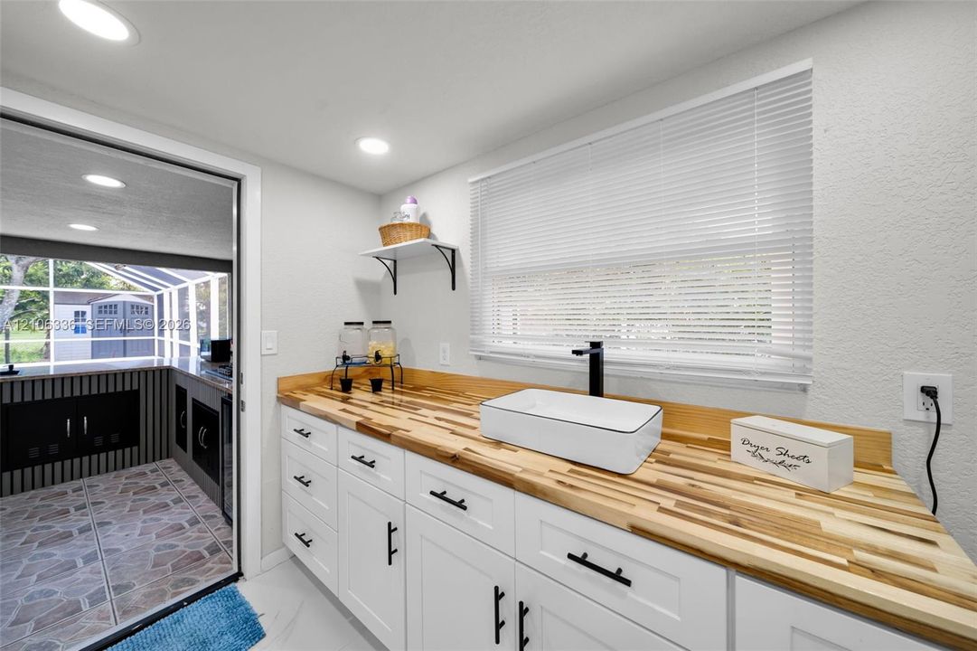 White cabinetry featuring butcher block countertops, a rectangular vessel sink with a matte black faucet, recessed lighting, and wall-mounted shelving
