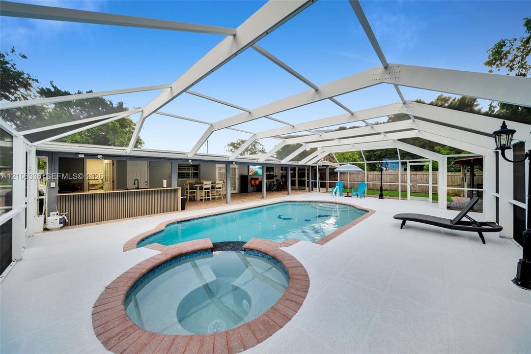 Screened-in pool area featuring a built-in spa with masonry surround, a covered wet bar, and light-toned hardscaping