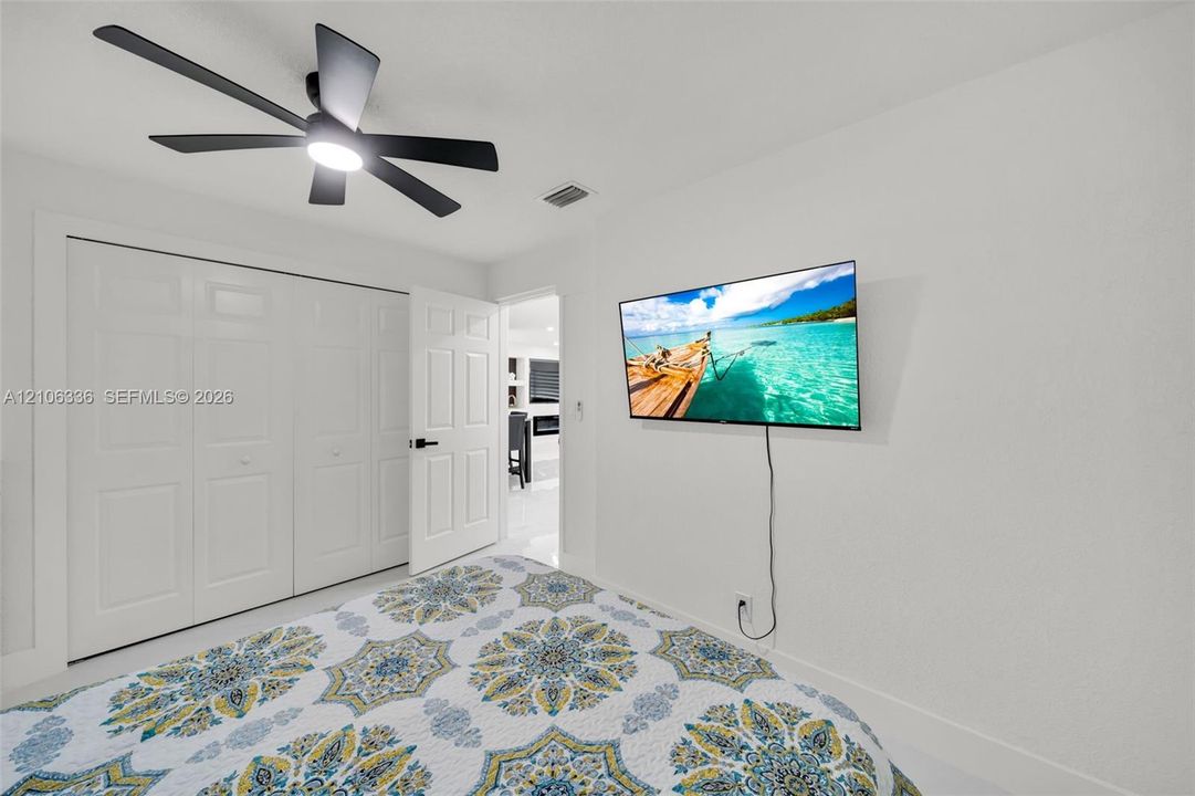 Neutral-toned room featuring a multi-blade ceiling fan with integrated lighting, bi-fold closet doors, and a solid-core interior door with matte black hardware