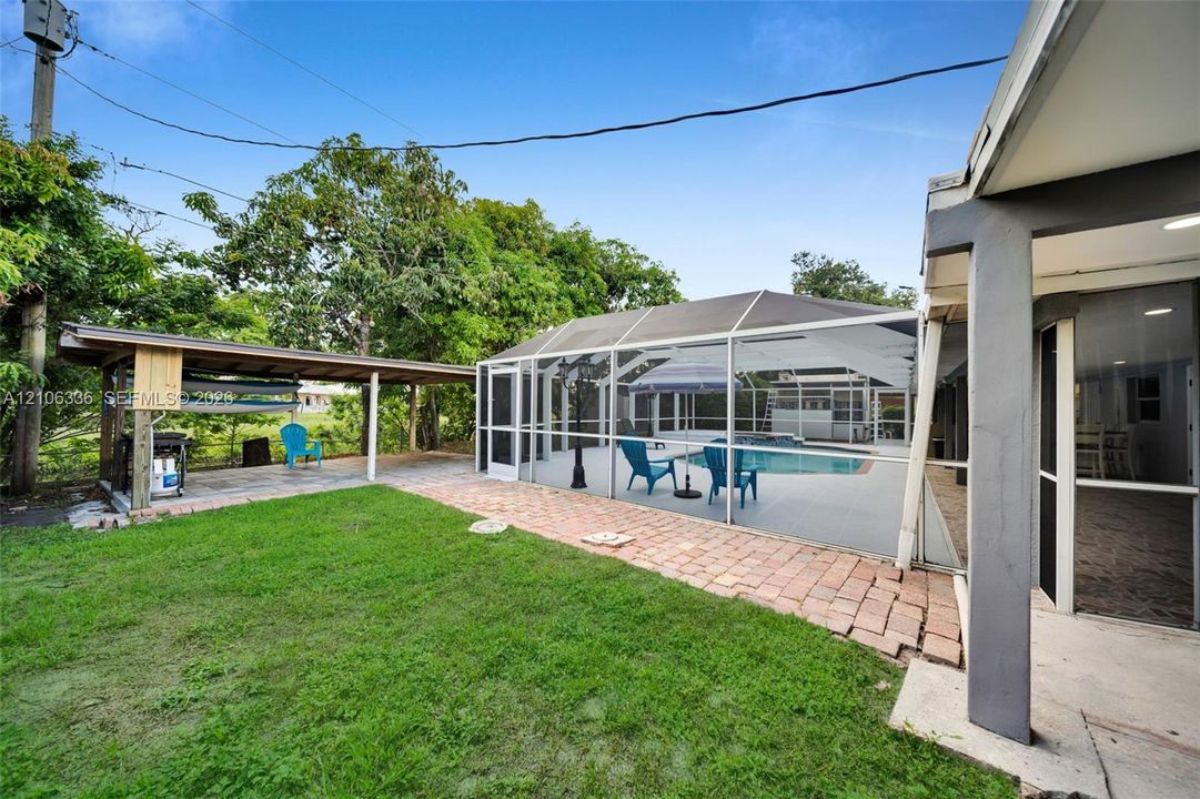 Screened-in pool, brick paver patio, and detached covered outdoor structure, situated on a lot with mature trees