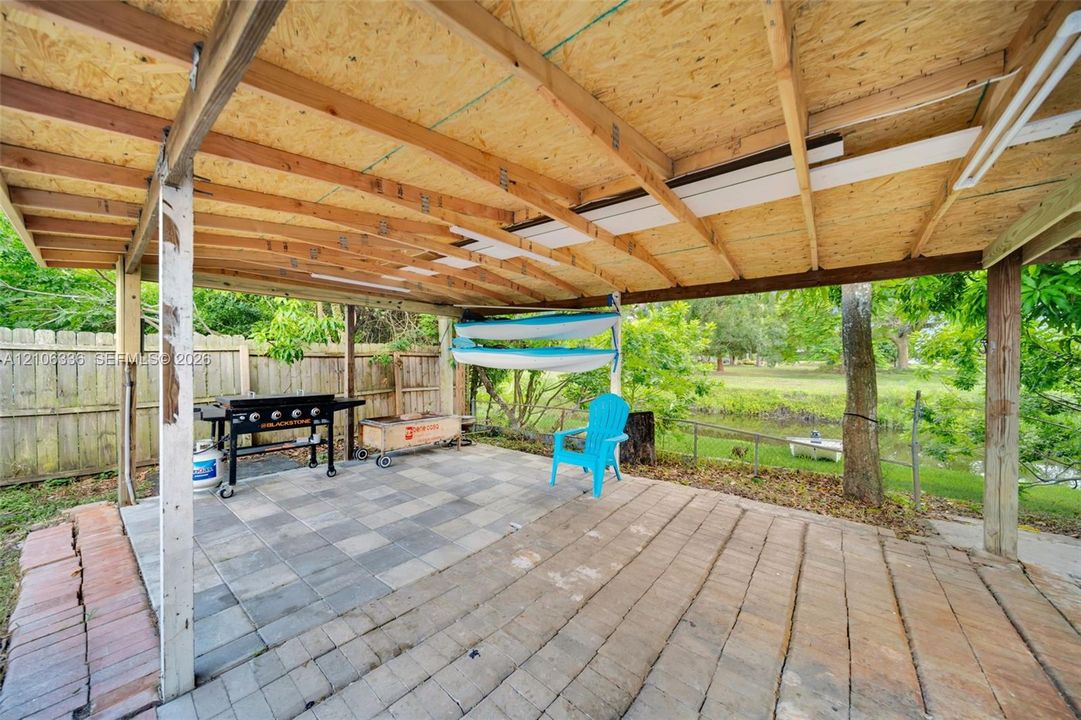 Covered outdoor living space featuring a wood-beam structure, stone paver flooring, and a fenced perimeter