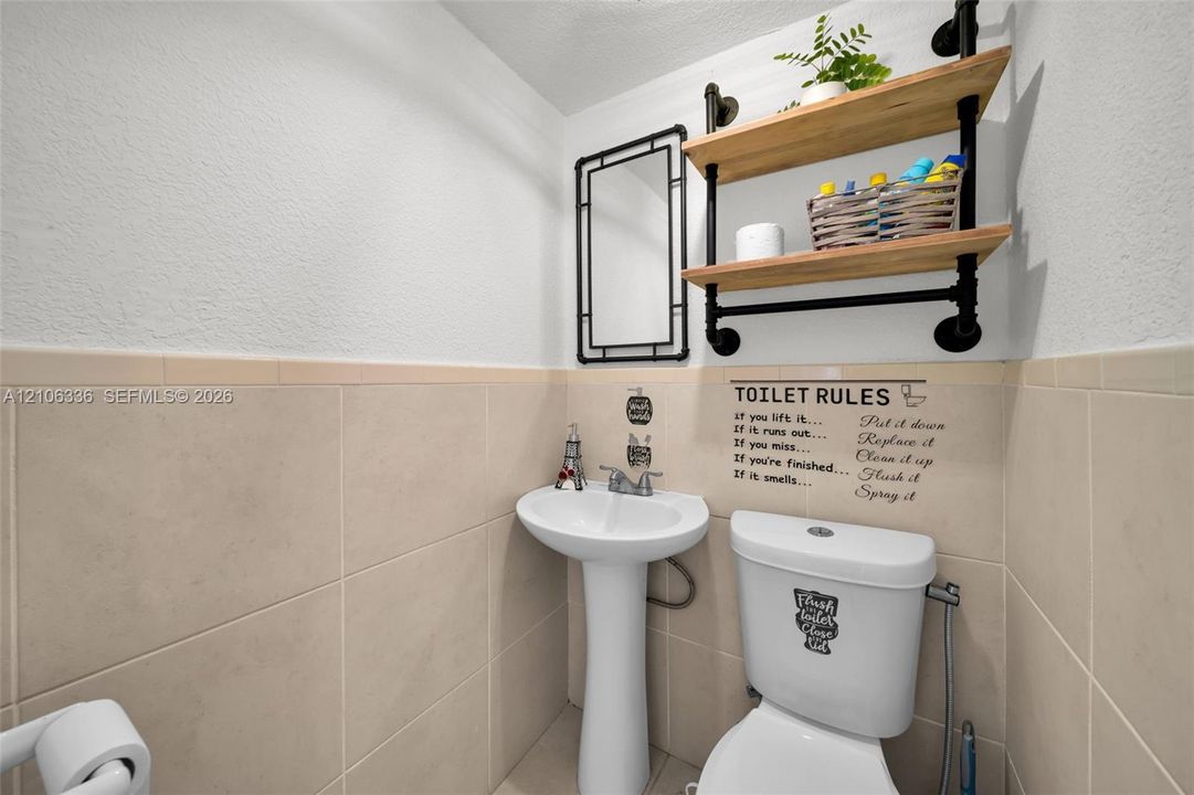 Pedestal sink with chrome faucet, beige ceramic wall tiling, and industrial-style shelving featuring wood-finish tiers and matte black hardware