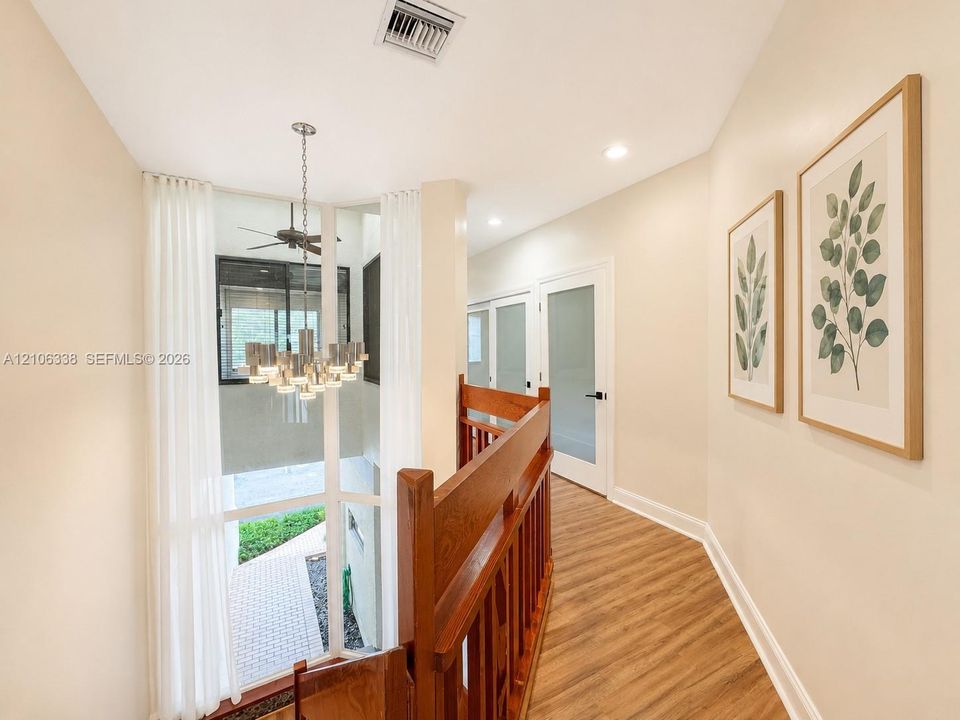Floor-to-ceiling windows, wood-finish flooring, multi-tiered metal chandelier, wooden stair railing, and frosted glass panel interior doors