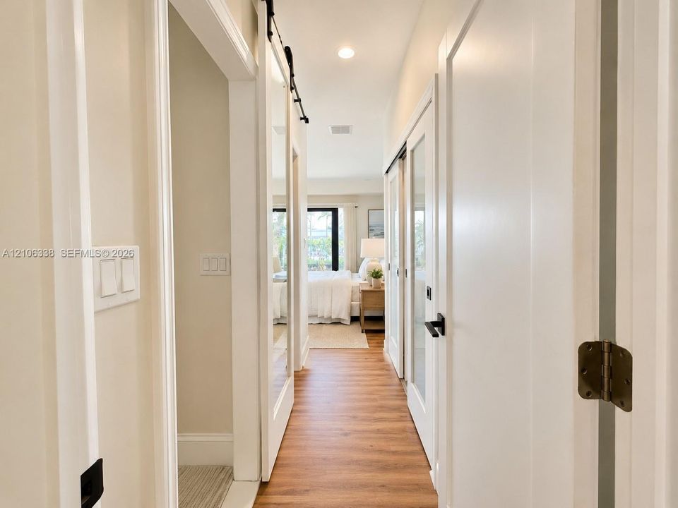 Hallway featuring wood-finish flooring, sliding barn door with full-length mirror, interior doors with frosted glass panels, and matte black hardware