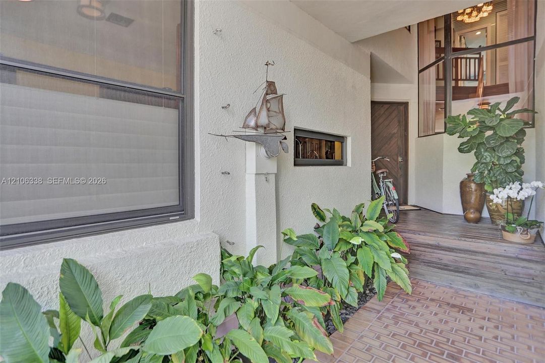 Covered entryway featuring a brick-paver porch, elevated wood-finish entry landing, multi-pane window configuration, and an oversized solid wood door with a diagonal plank design