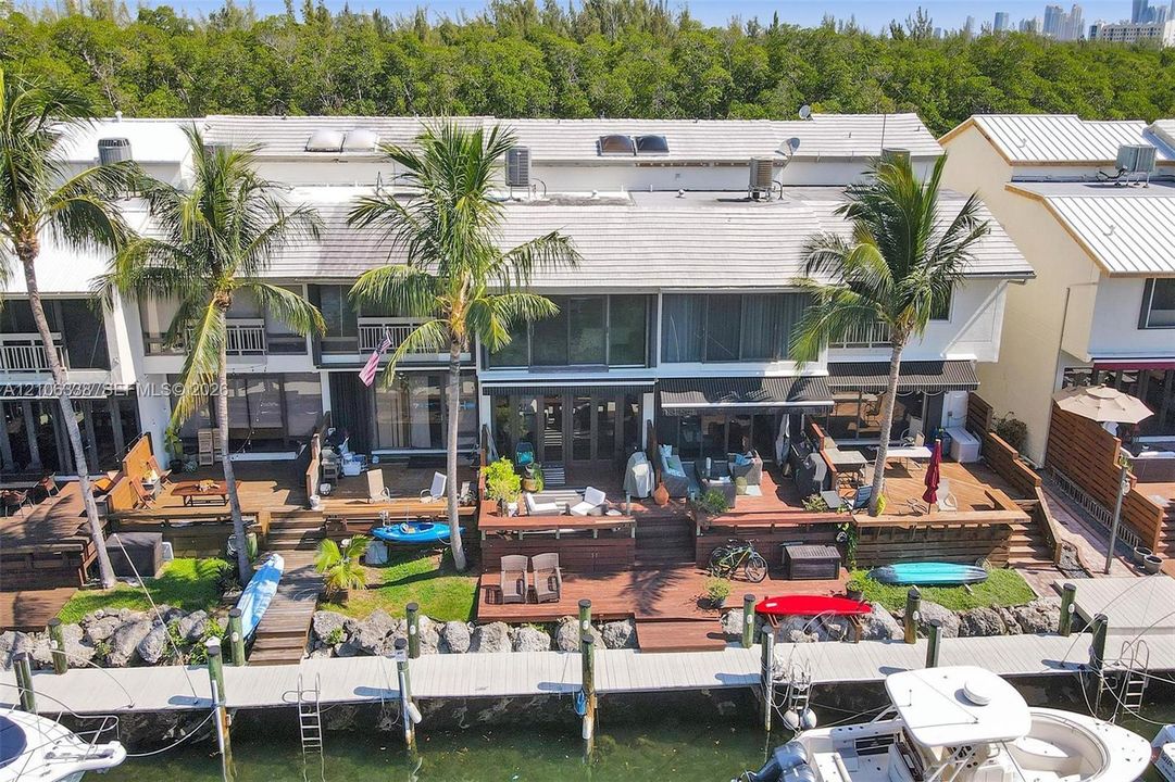 Waterfront multi-story residence featuring tiered wood decking, private deep-water dockage, mature palm trees, and stone-reinforced bulkheading