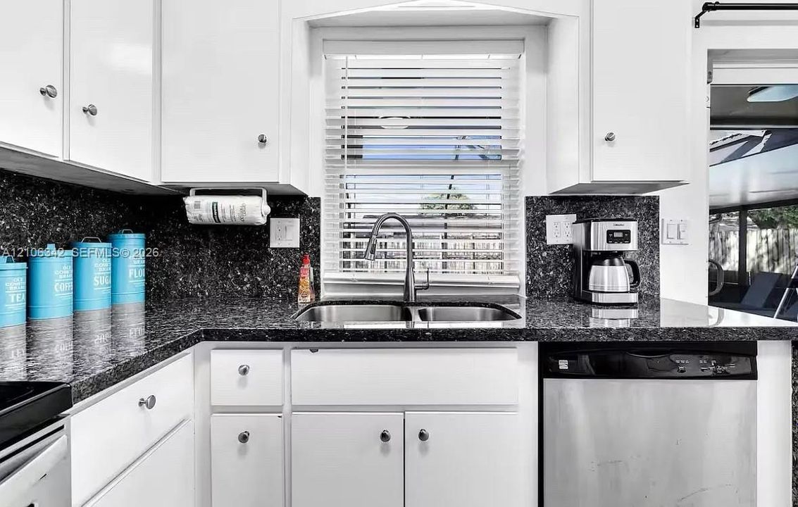 Kitchen featuring white shaker-style cabinetry, dark stone countertops, dual-basin stainless steel sink with high-arch faucet, and stainless steel dishwasher